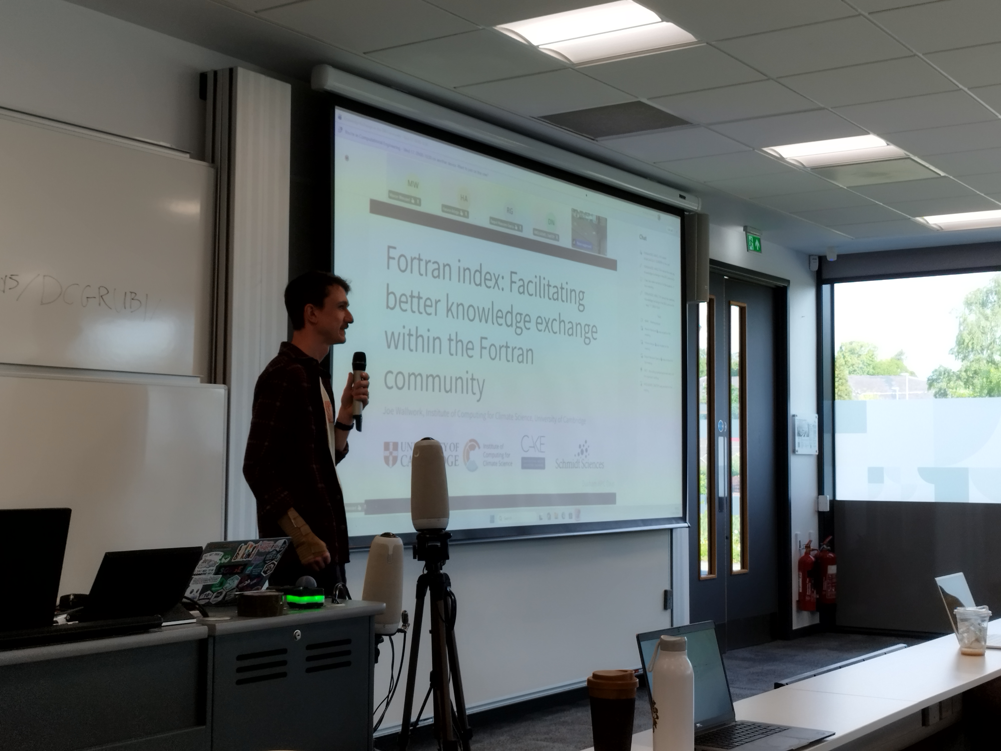 Man (Joe) in red checkered shirt giving a talk in front of slides titled 'Fortran Index - Facilitating better knowledge exchange within the Fortran Community' 